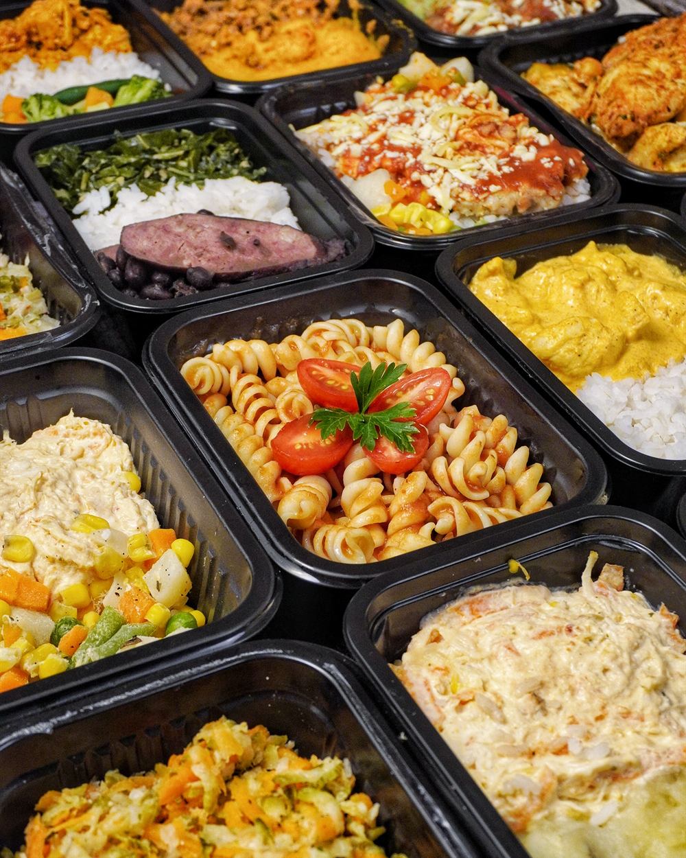 Dezenas de marmitas variadas alinhadas, com massas, frango, arroz e legumes